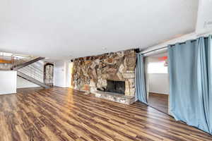 Unfurnished family room with a textured ceiling, wood-type flooring, and a stone fireplace