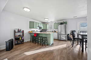 Kitchen with kitchen peninsula, vinyl flooring, green cabinets, appliances with stainless steel finishes, and a kitchen breakfast bar