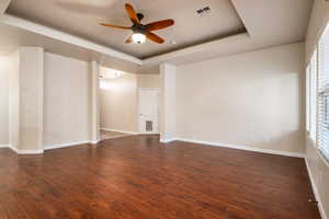 Unfurnished room with ceiling fan, dark hardwood / wood-style flooring, and a tray ceiling