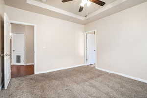 Carpeted spare room featuring ceiling fan and a tray ceiling