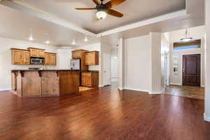 Kitchen with appliances with stainless steel finishes, a kitchen bar, dark wood-type flooring, a raised ceiling, and ceiling fan