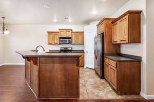 Kitchen featuring stainless steel appliances, pendant lighting, a center island with sink, and sink