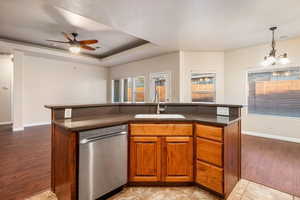 Kitchen featuring dishwasher, a tray ceiling, sink, light tile patterned floors, and a center island with sink