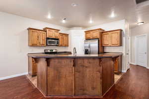 Kitchen featuring a kitchen bar, dark hardwood / wood-style floors, stainless steel appliances, and a center island with sink