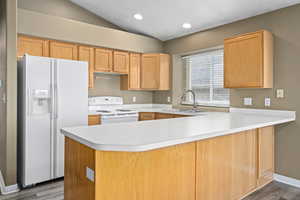 Kitchen with vaulted ceiling, kitchen peninsula, sink, white appliances, and light wood-type flooring