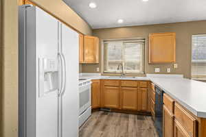 Kitchen with kitchen peninsula, a healthy amount of sunlight, white appliances, light hardwood / wood-style flooring, and sink