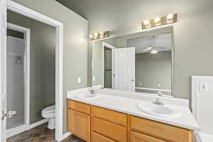 Bathroom featuring toilet, ceiling fan, walk in shower, and vanity