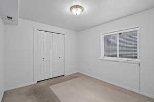 Unfurnished bedroom with light carpet, a closet, and a textured ceiling