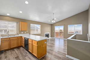 Kitchen featuring kitchen peninsula, black dishwasher, a fireplace, vaulted ceiling, and sink