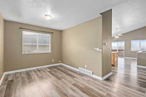 Empty room with lofted ceiling, light wood-type flooring, a textured ceiling, and ceiling fan