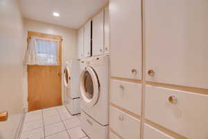 Clothes washing area with cabinets, light tile patterned floors, and washer and clothes dryer