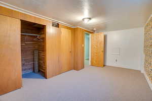 Unfurnished bedroom with light carpet, a closet, wooden walls, and a textured ceiling