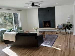 Living room featuring ceiling fan, a tiled fireplace, and light wood-type flooring