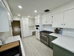 Kitchen with high end stainless steel range, white oven, decorative backsplash, and white cabinetry