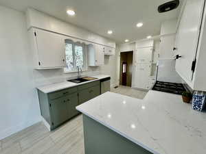 Kitchen with green cabinetry, white cabinetry, backsplash, and sink