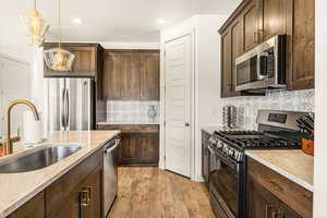 Kitchen featuring sink, light stone counters, light wood-type flooring, pendant lighting, and stainless steel appliances