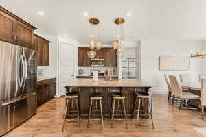 Kitchen featuring light stone counters, stainless steel appliances, hanging light fixtures, and a center island with sink