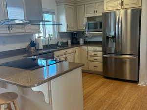 Kitchen featuring island range hood, a breakfast bar area, appliances with stainless steel finishes, light hardwood / wood-style floors, and sink