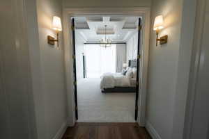 Hallway featuring ornamental molding, a chandelier, a tray ceiling, and dark wood finished floors
