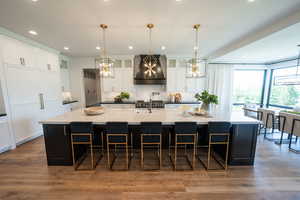Kitchen with premium range hood, tasteful backsplash, a large island with sink, a breakfast bar, and white cabinets