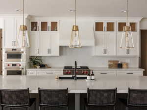Kitchen featuring white cabinetry, glass insert cabinets, decorative light fixtures, a spacious island, and recessed lighting