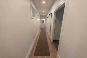 Hallway with a barn door, recessed lighting, and wood finished floors