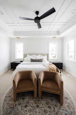 Carpeted bedroom featuring ceiling fan, multiple windows, crown molding, and coffered ceiling