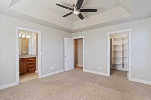 Unfurnished bedroom featuring ceiling fan, a walk in closet, connected bathroom, and a raised ceiling