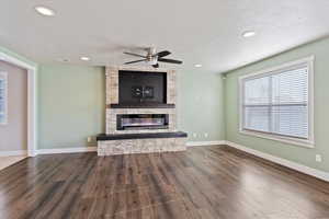 Unfurnished living room featuring a textured ceiling, ceiling fan, hardwood / wood-style floors, and a stone fireplace