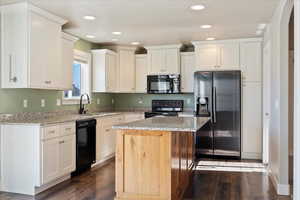 Kitchen with black appliances, a center island, dark wood-type flooring, sink, and light stone counters