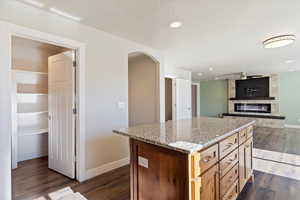 Kitchen with ceiling fan, a fireplace, a center island, light stone countertops, and dark hardwood / wood-style flooring