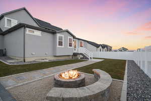 Back house at dusk with cooling unit, a yard, and a fire pit