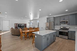 Kitchen featuring gray cabinets, appliances with stainless steel finishes, hanging light fixtures, a kitchen island, and light hardwood / wood-style flooring