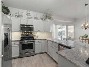 Kitchen with decorative light fixtures, white cabinetry, stainless steel appliances, decorative backsplash, and sink