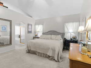 Bedroom featuring light carpet, ensuite bathroom, and vaulted ceiling