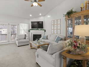 Living room featuring vaulted ceiling, ceiling fan, a tiled fireplace, and carpet floors