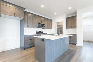 Kitchen featuring sink, appliances with stainless steel finishes, a kitchen island with sink, hardwood / wood-style floors, and dark brown cabinetry