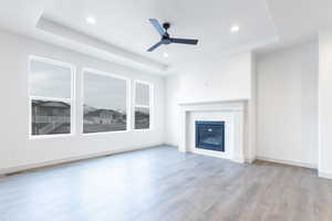 Unfurnished living room with ceiling fan, light hardwood / wood-style floors, and a tray ceiling