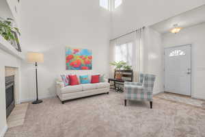 Living room featuring light colored carpet, a fireplace, and a high ceiling