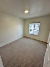 Carpeted empty room featuring a textured ceiling, baseboards, and visible vents