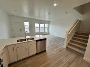 Kitchen with stainless steel dishwasher, light wood-style flooring, a textured ceiling, white cabinetry, and a sink
