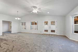 Unfurnished living room featuring vaulted ceiling, ceiling fan with notable chandelier, french doors, and carpet floors