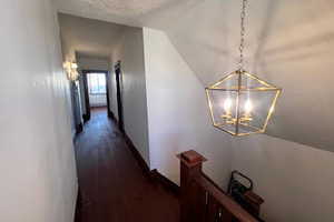 Hallway with dark wood-type flooring and a chandelier