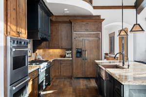 Kitchen featuring stainless steel appliances, decorative backsplash, light stone counters, and decorative light fixtures