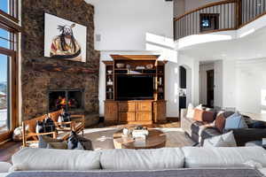 Living room with a high ceiling, a healthy amount of sunlight, a stone fireplace, and hardwood / wood-style floors