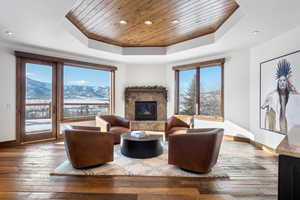 Living room featuring wood-type flooring, a mountain view, a tray ceiling, a tiled fireplace, and wooden ceiling