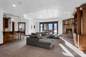 Carpeted living room featuring a tray ceiling, a stone fireplace, and bar area