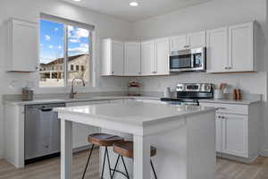 Kitchen with sink, appliances with stainless steel finishes, white cabinetry, a center island, and a kitchen bar
