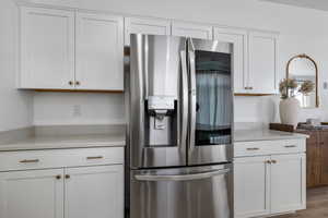 Kitchen with stainless steel fridge, hardwood / wood-style floors, and white cabinets