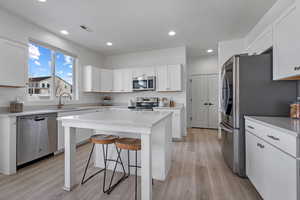 Kitchen with a breakfast bar, sink, white cabinets, a center island, and stainless steel appliances